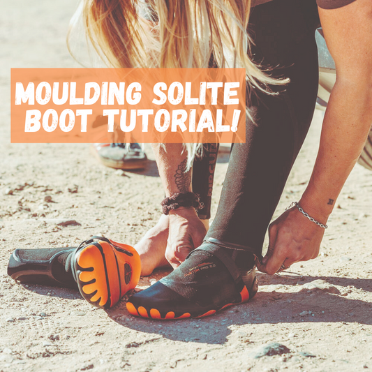 Person putting on Solite wetsuit boot on sandy ground, orange sole visible, boot tutorial.