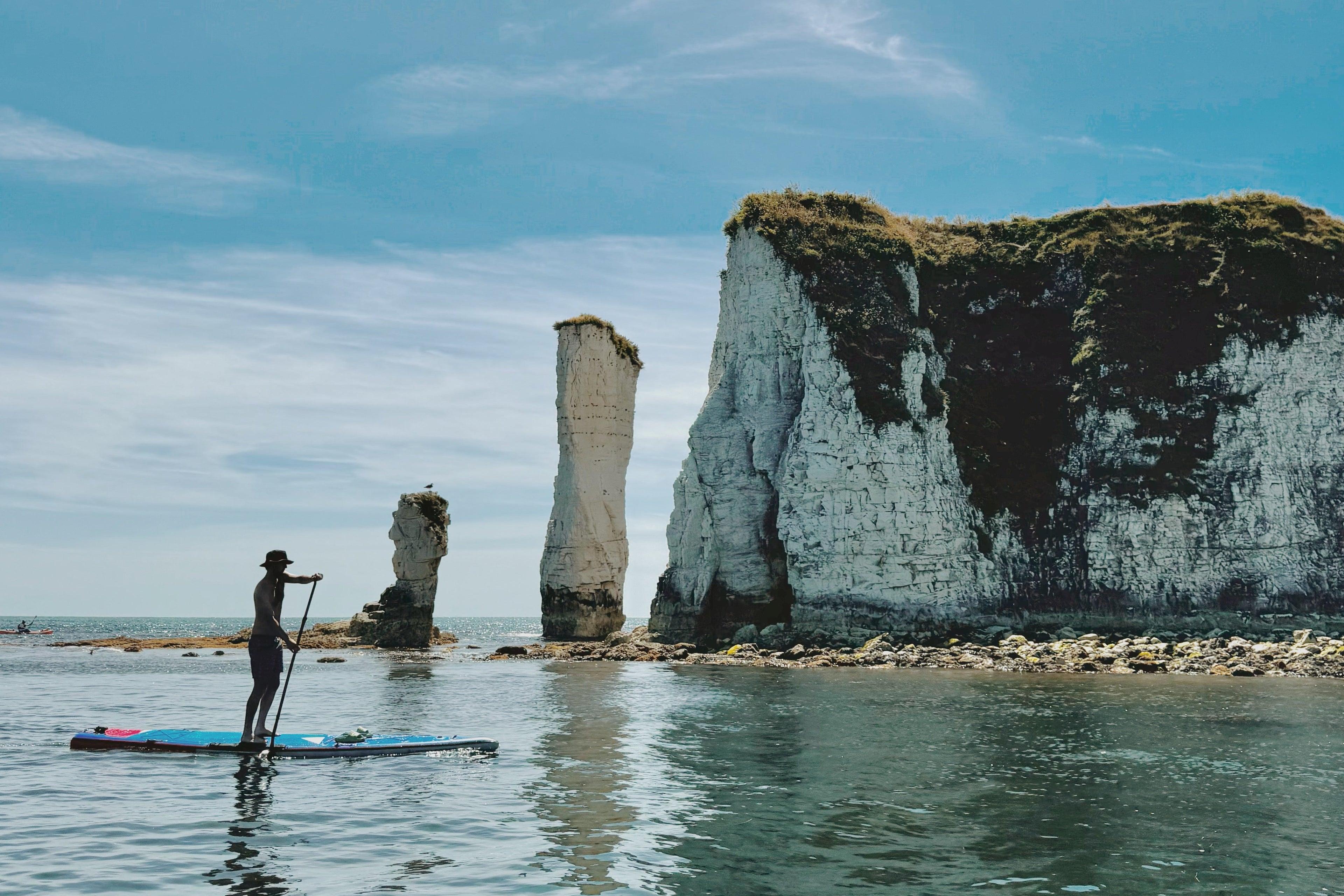 Person paddleboarding near chalk cliffs on a clear day